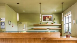A reception desk with a wooden finish, pendant lights, a framed abstract painting, and a window with a view. - Gaia Hotel & Spa Redding, an Ascend Collection Hotel (Anderson)