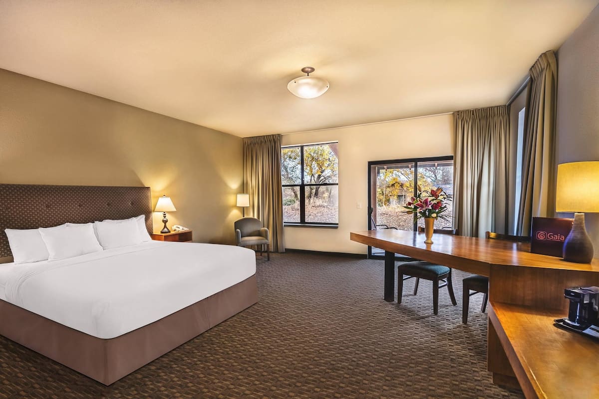 Habitación de hotel con una cama grande, un escritorio, una silla, una lámpara y una ventana con cortinas.