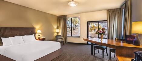 A hotel room with a large bed, a desk, a chair, a lamp, and a window with curtains.