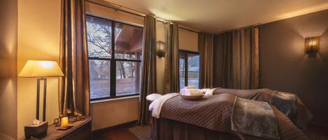 Habitación de hotel con cama, mesita de noche, lámpara y vista a los árboles por la ventana.