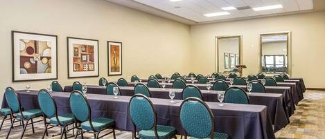 A conference room with rows of tables and chairs, framed artwork on the walls, and a carpeted floor.