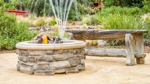 A stone fire pit with a fire, surrounded by a wooden bench and a stone bench. - Gaia Hotel & Spa Redding, an Ascend Collection Hotel (Anderson)