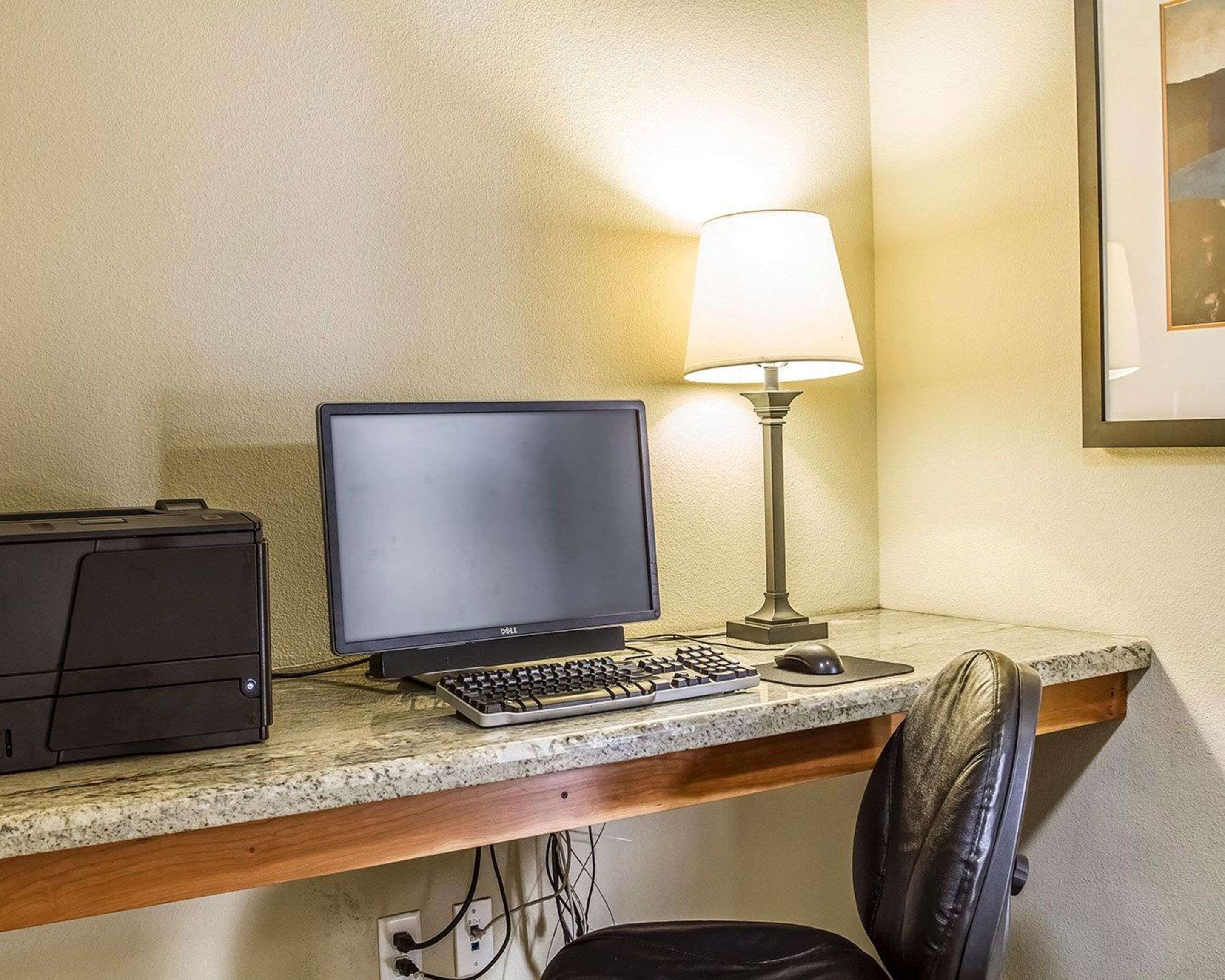 Een werkplek in een hotel, met een computer, toetsenbord, muis en een lamp.