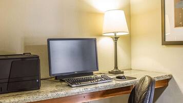 Un espacio de trabajo en un hotel con un ordenador de escritorio, teclado, ratón y una lámpara.