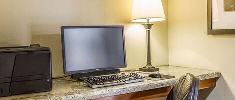 Een werkplek in een hotel, met een computer, toetsenbord, muis en een lamp.
