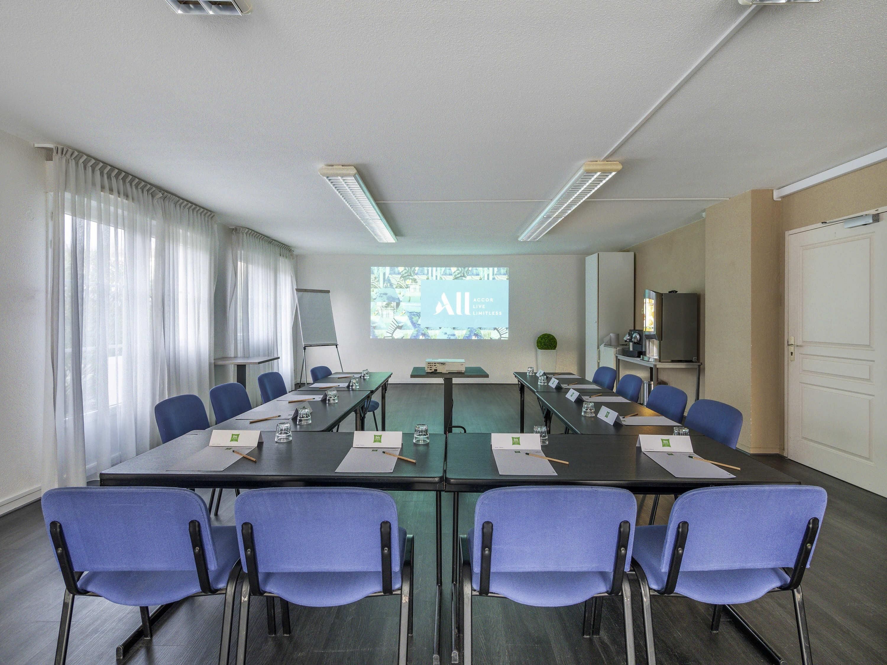 Une salle de conférence avec une longue table, des chaises bleues, un écran de projection et un tableau blanc.