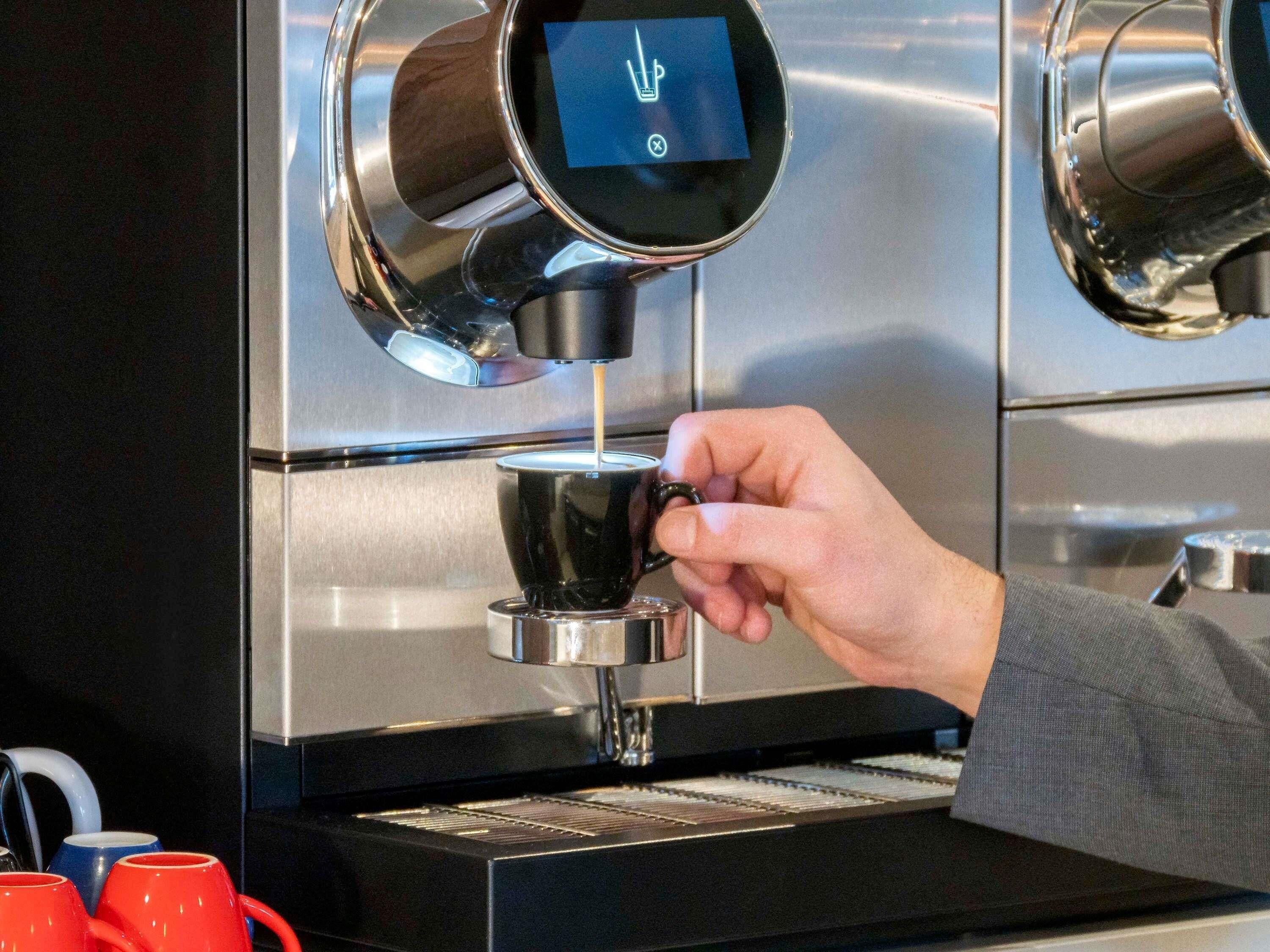 Une main tenant une tasse sous une machine à café dotée d’un écran numérique.
