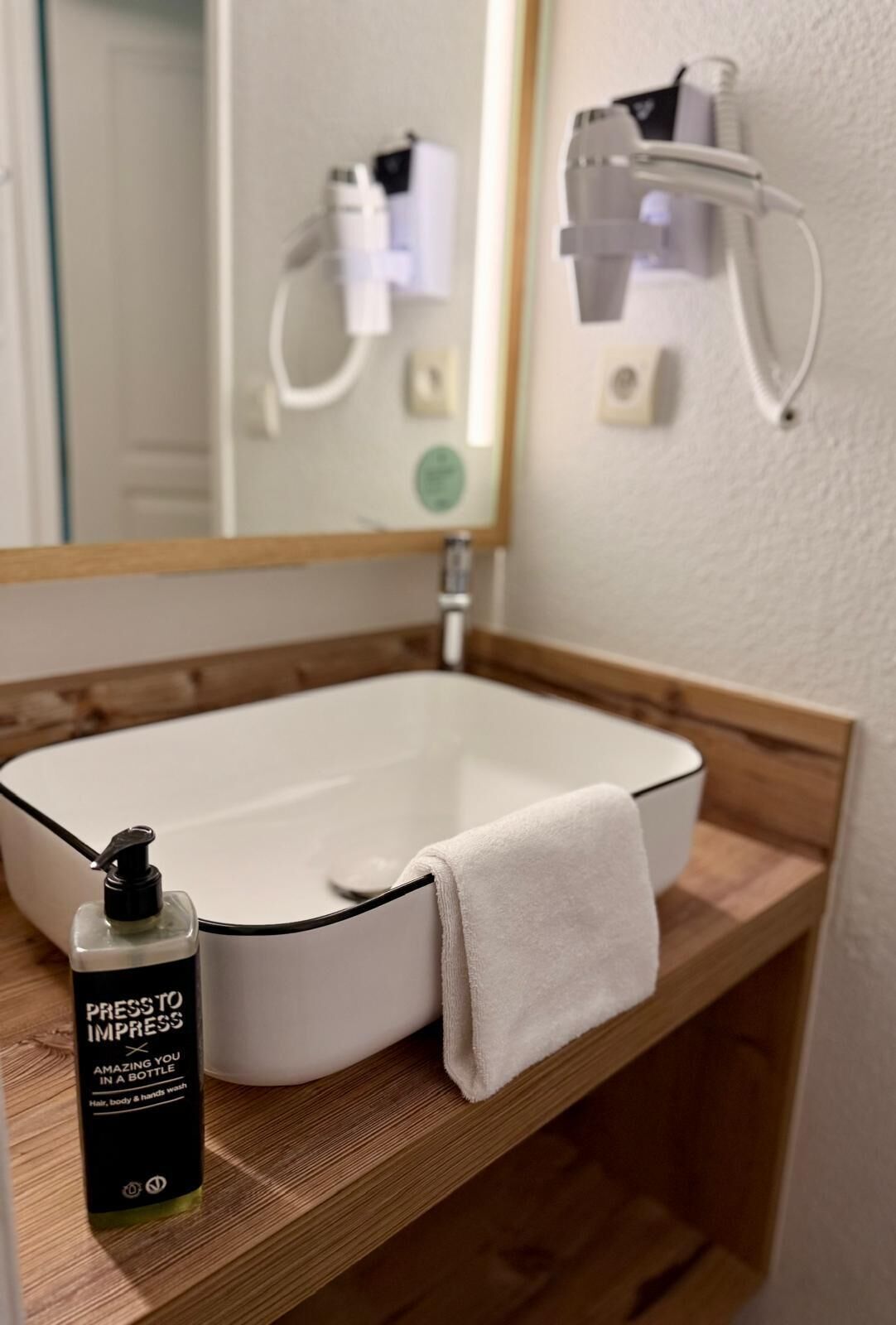 A bathroom with a white sink, a mirror, a towel, and a bottle of hand soap.