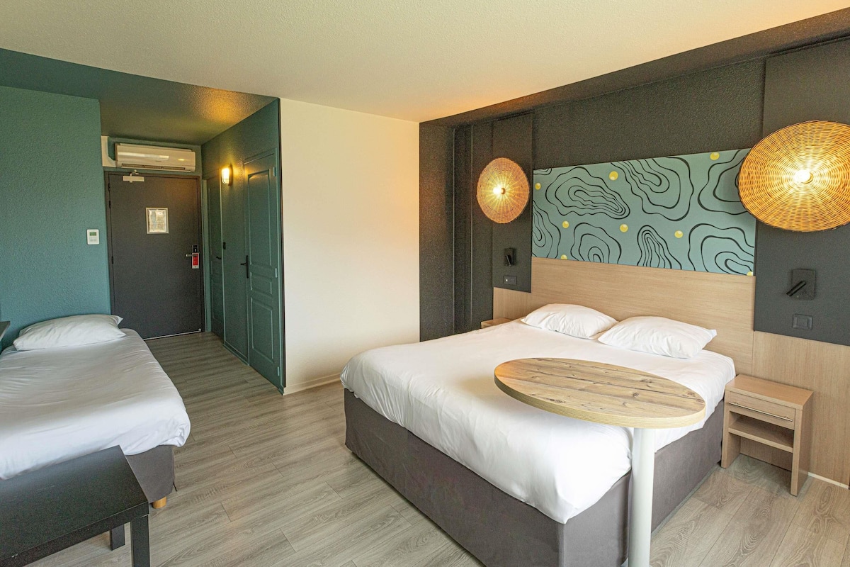 Une chambre d’hôtel avec un lit, une table de chevet et une lampe fixée au mur.
