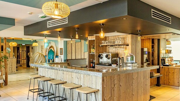 A modern kitchen with a central island, bar stools, and a coffee machine. - Hôtel ibis Styles Marennes Oleron (Marennes-Hiers-Brouage)