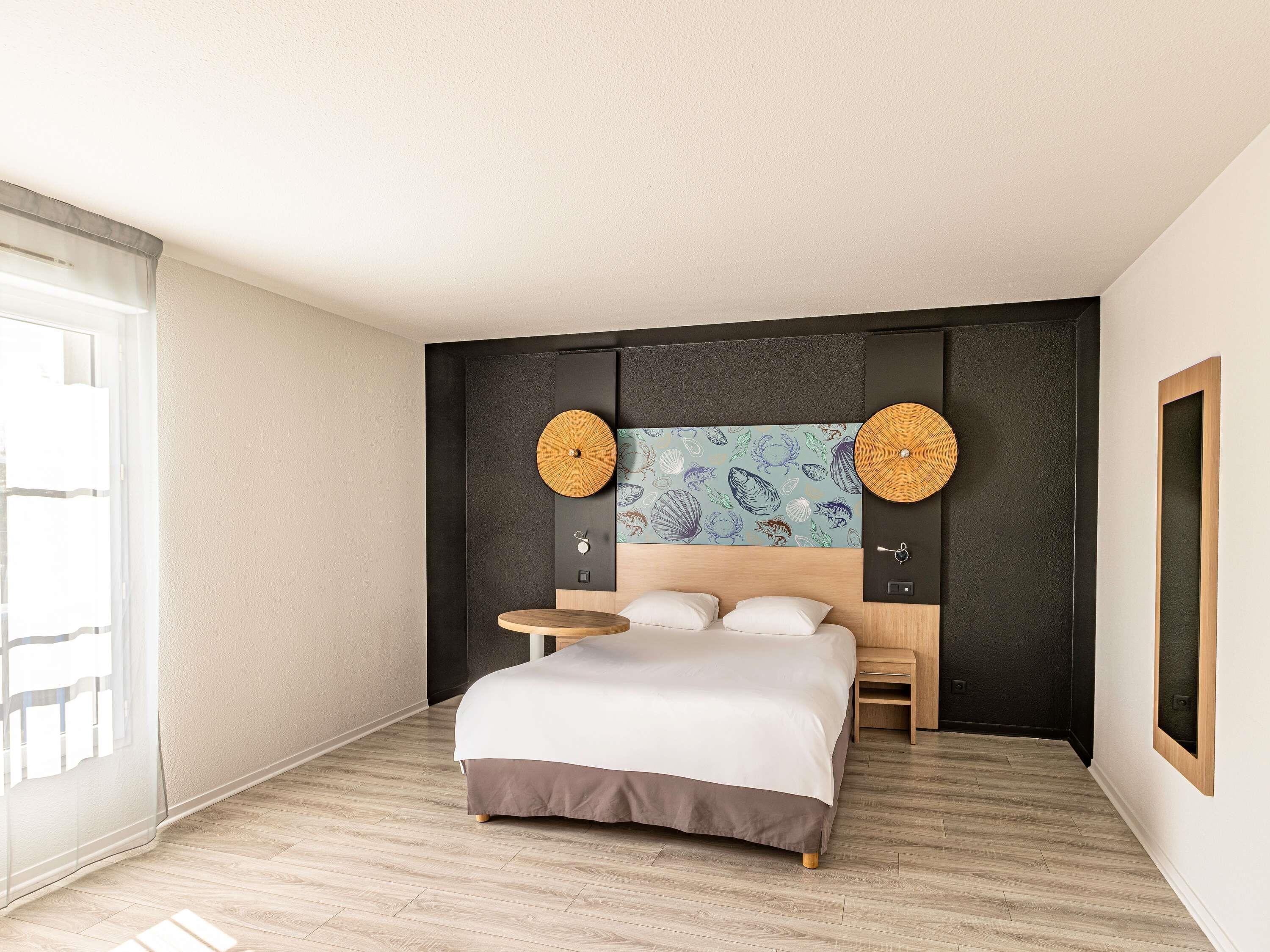 A modern hotel room with a bed, a round table, and a large wall art piece.