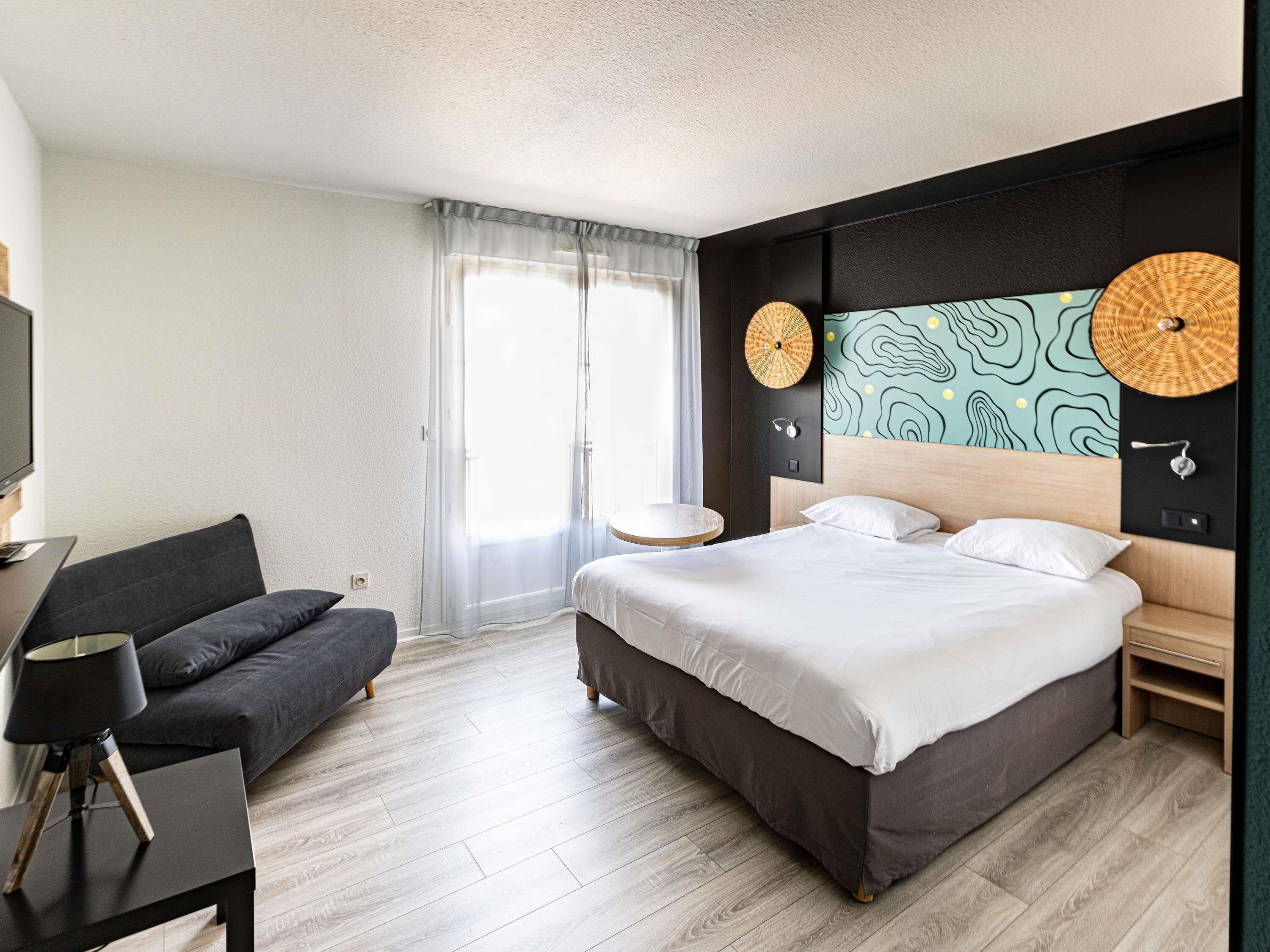 A modern hotel room with a large bed, a sofa, a desk, and a TV.