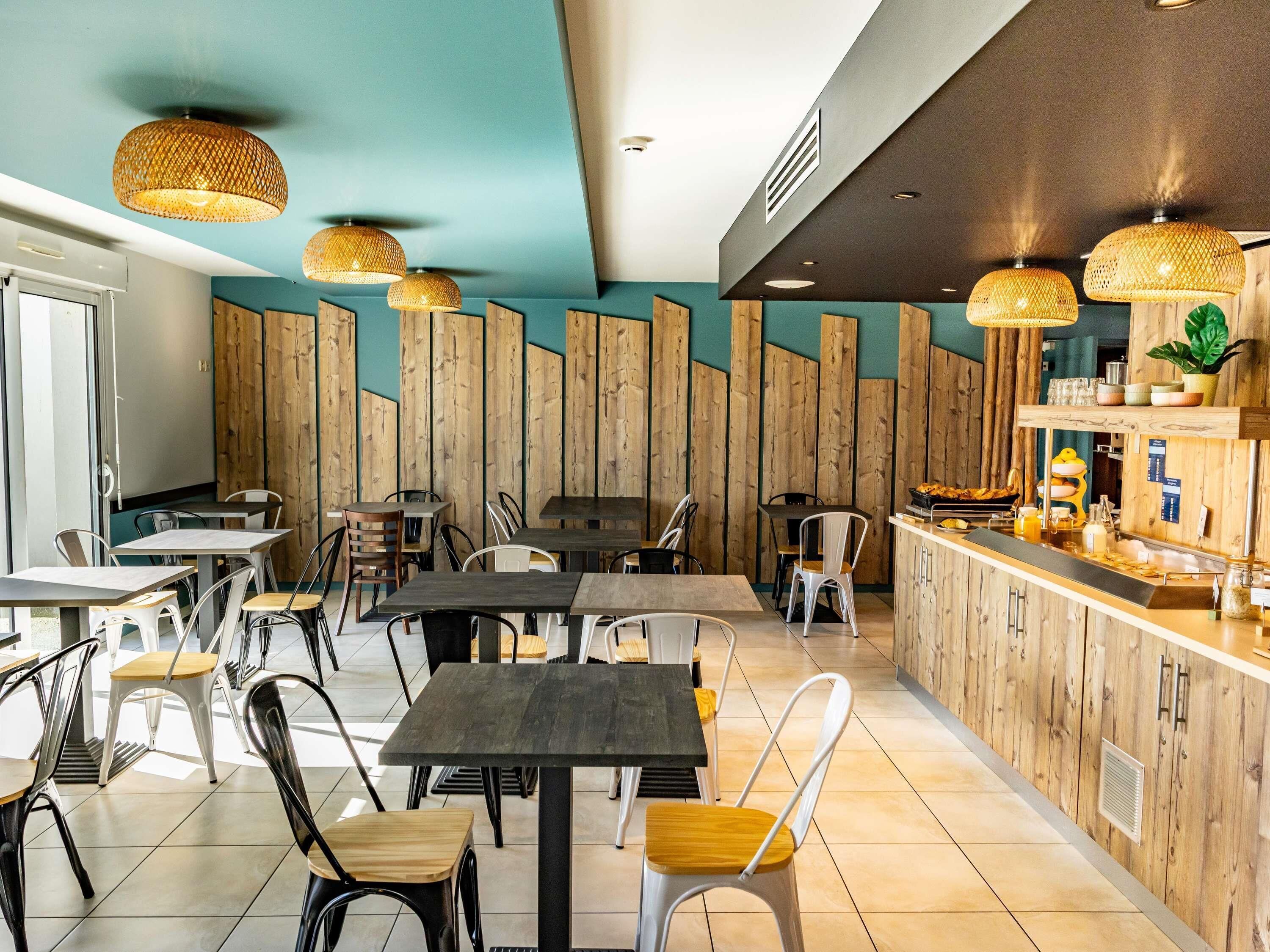 A modern restaurant interior with wooden panel walls, black and white chairs, and woven pendant lights.