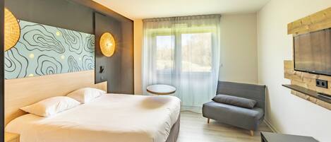Una habitación de hotel moderna con una cama grande, un sofá, una pequeña mesa, un televisor y una mesita redonda.