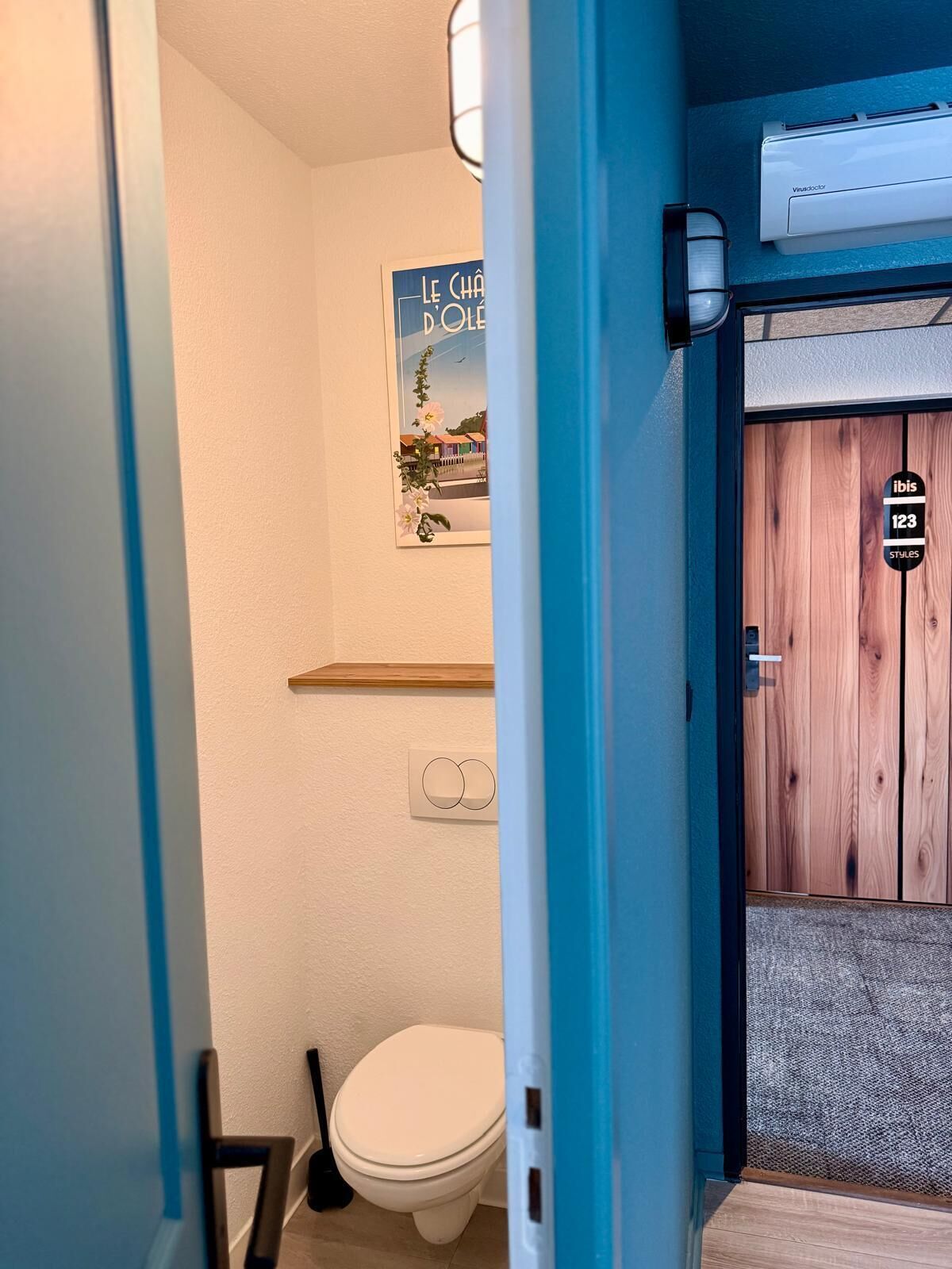 Un baño con inodoro blanco, puerta de madera y un cartel en la pared.