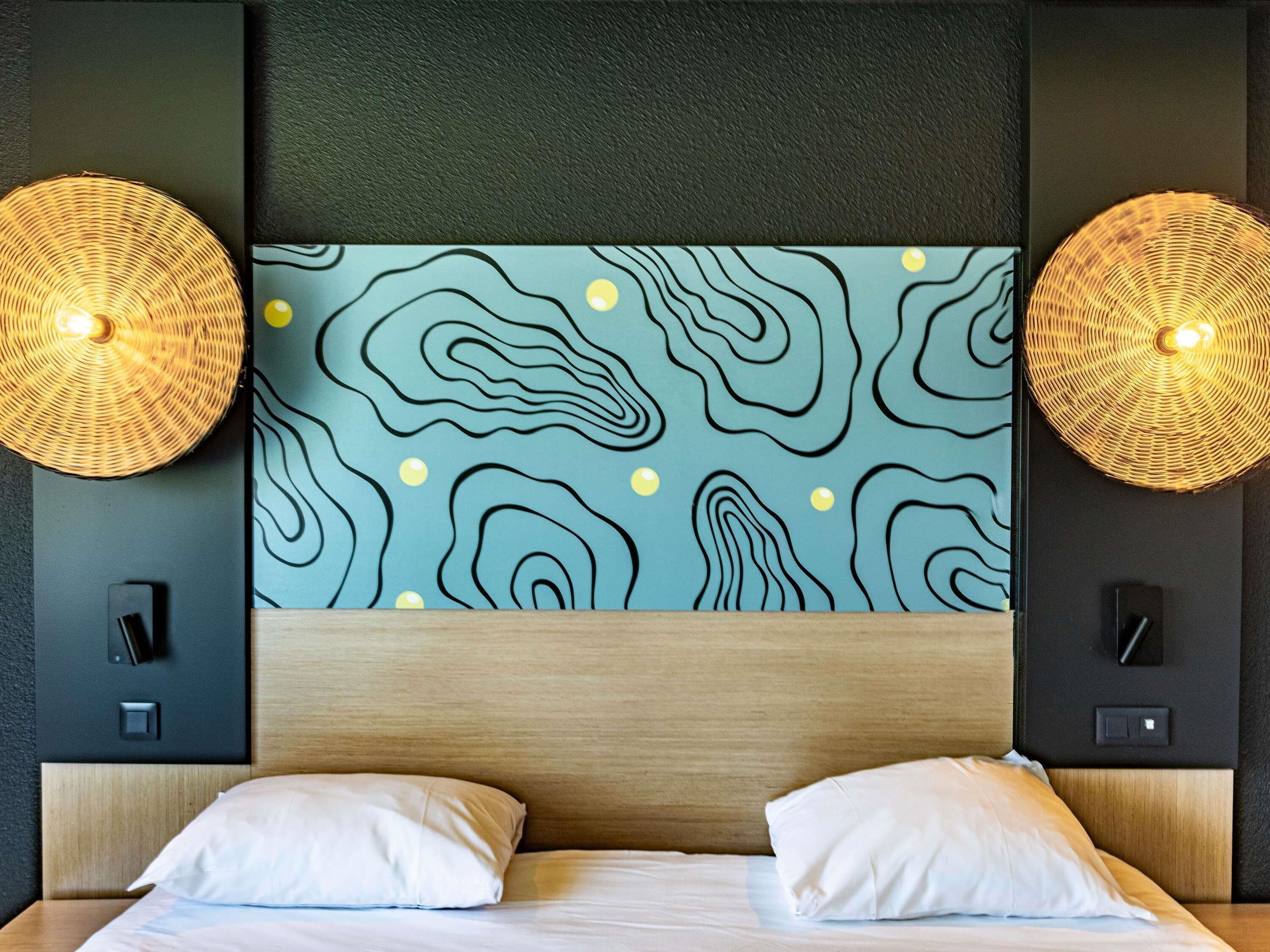 A hotel room with a wooden headboard, a wall with a wavy pattern, and two wall-mounted lamps.