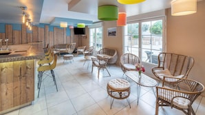 A modern interior with a bar area, wicker furniture, and large windows. - Hôtel ibis Styles Marennes Oleron (Marennes-Hiers-Brouage)