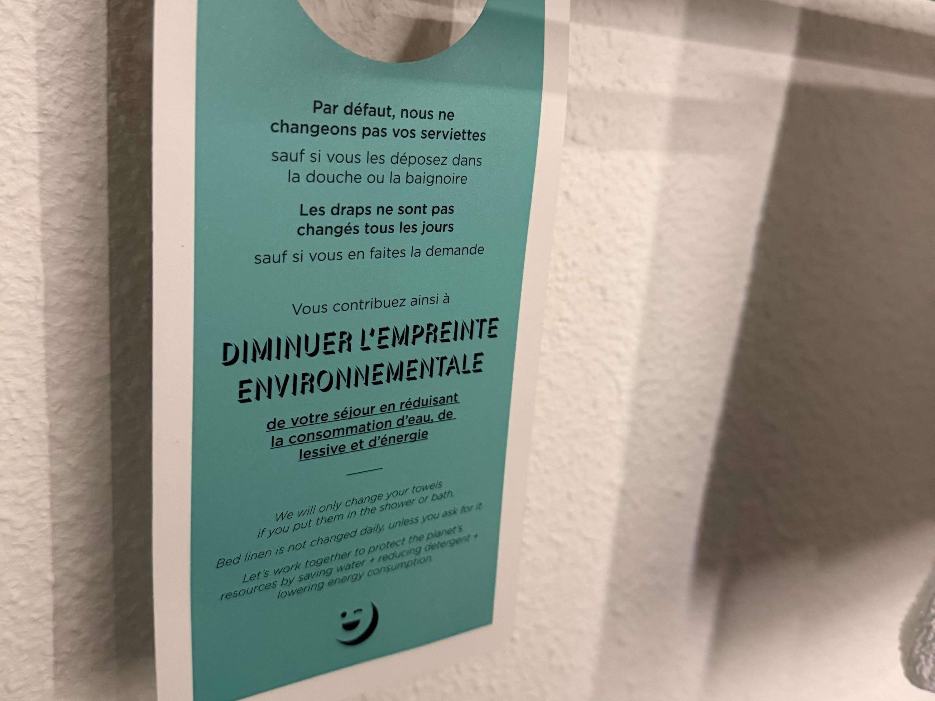 A teal-colored informational sign with text in French, likely providing guidelines on towel usage and environmental conservation in a hotel setting.