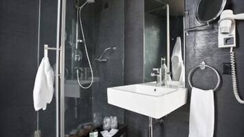 A modern bathroom with a glass-enclosed shower, a white sink, and a hairdryer mounted on the wall.