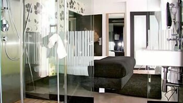 Un baño moderno con mampara de vidrio, una bañera negra y un lavamanos blanco con espejo.