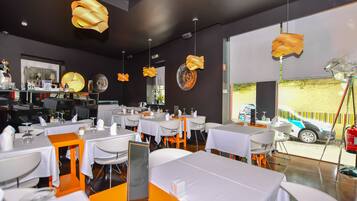 Un interior de restaurante moderno con mesas blancas, detalles en naranja y originales lámparas colgantes.