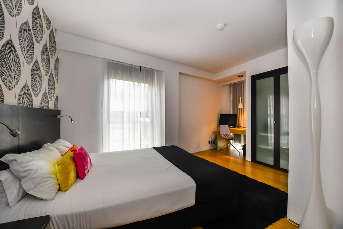Ein modernes Hotelzimmer mit einem großen Bett, einem Schreibtisch und Blick auf die Stadt durch das Fenster.