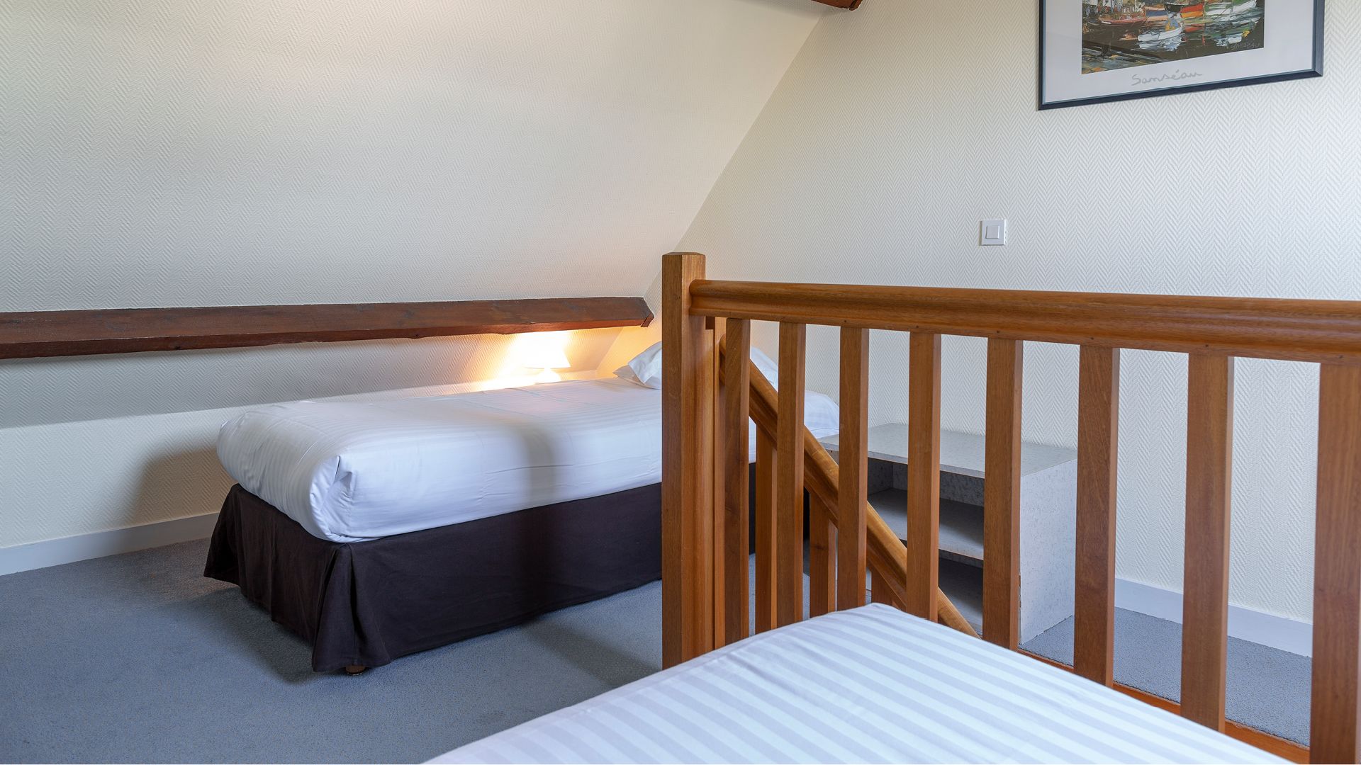 Une petite chambre à coucher, bien rangée, avec un lit simple, une tête de lit en bois et un petit escalier.