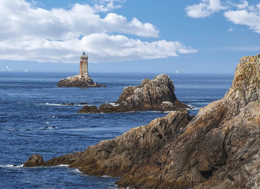 Paisaje costero con un faro en una pequeña isla, acantilados rocosos y el mar.