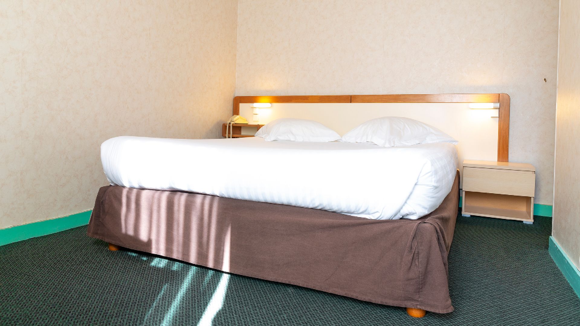 A hotel room with a bed, a bedside table, and a nightstand.