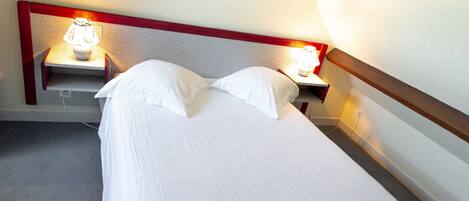 Una cama individual con ropa blanca, en una habitación con cabecera de madera y dos mesitas de noche con lámparas.