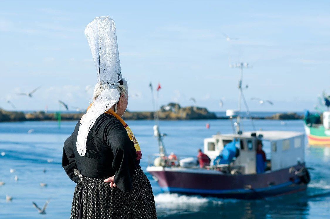 A person standing by a body of water with boats and seagulls in the background.