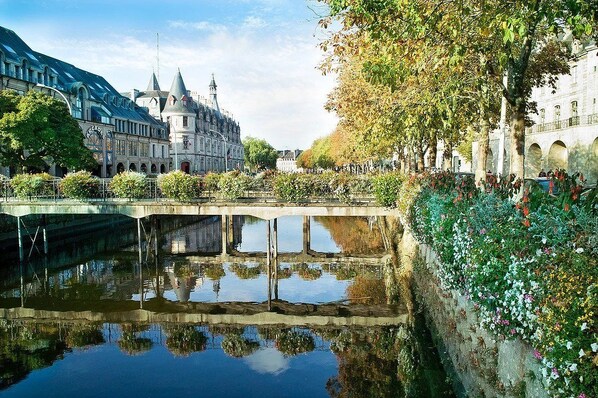 Un edificio histórico con una torre del reloj, un puente sobre un canal y un jardín lleno de flores.