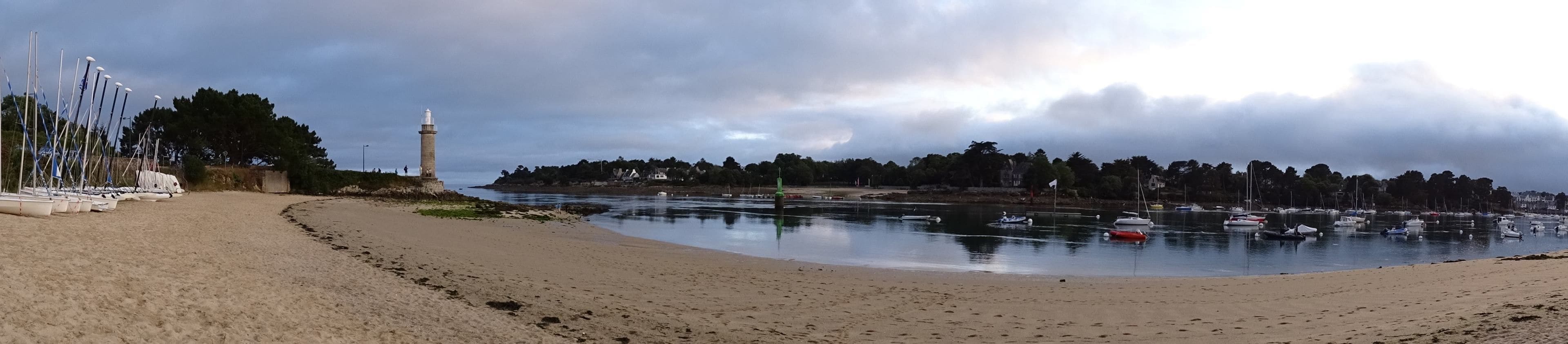 Une plage avec un phare, des bateaux et une mer calme.