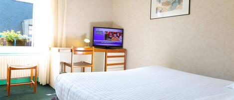 A hotel room with a bed, a desk with a television, a chair, and a window with curtains.