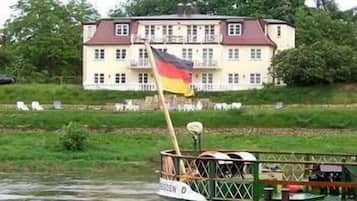 A boat with a flag, a large building with multiple windows and balconies, and a grassy area in the background.