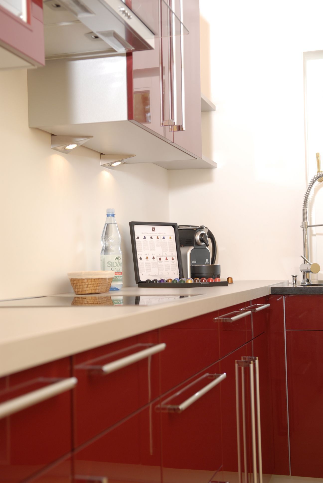 A kitchen with red cabinets, a coffee machine, a water bottle, and a menu board.