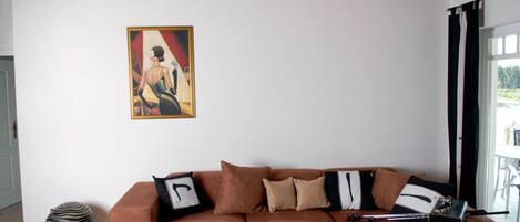 Uma sala de estar com um sofá marrom, uma mesa de centro de vidro e um quadro na parede.