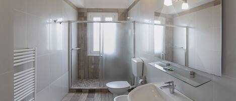 Un baño moderno con cabina de ducha de vidrio, dos inodoros, un lavamanos y un espejo grande.
