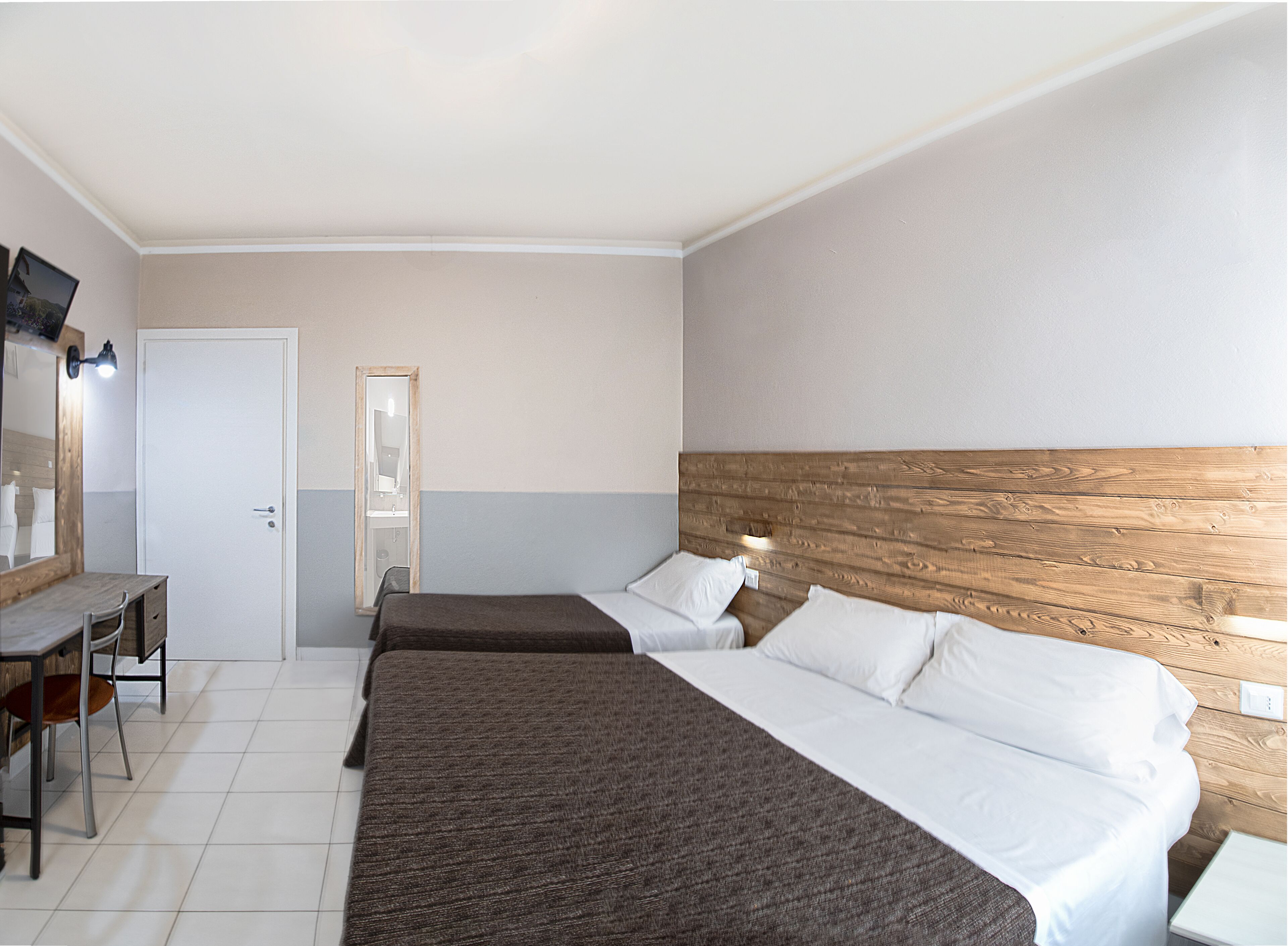 A hotel room with two beds, a desk, a mirror, and a wooden headboard.