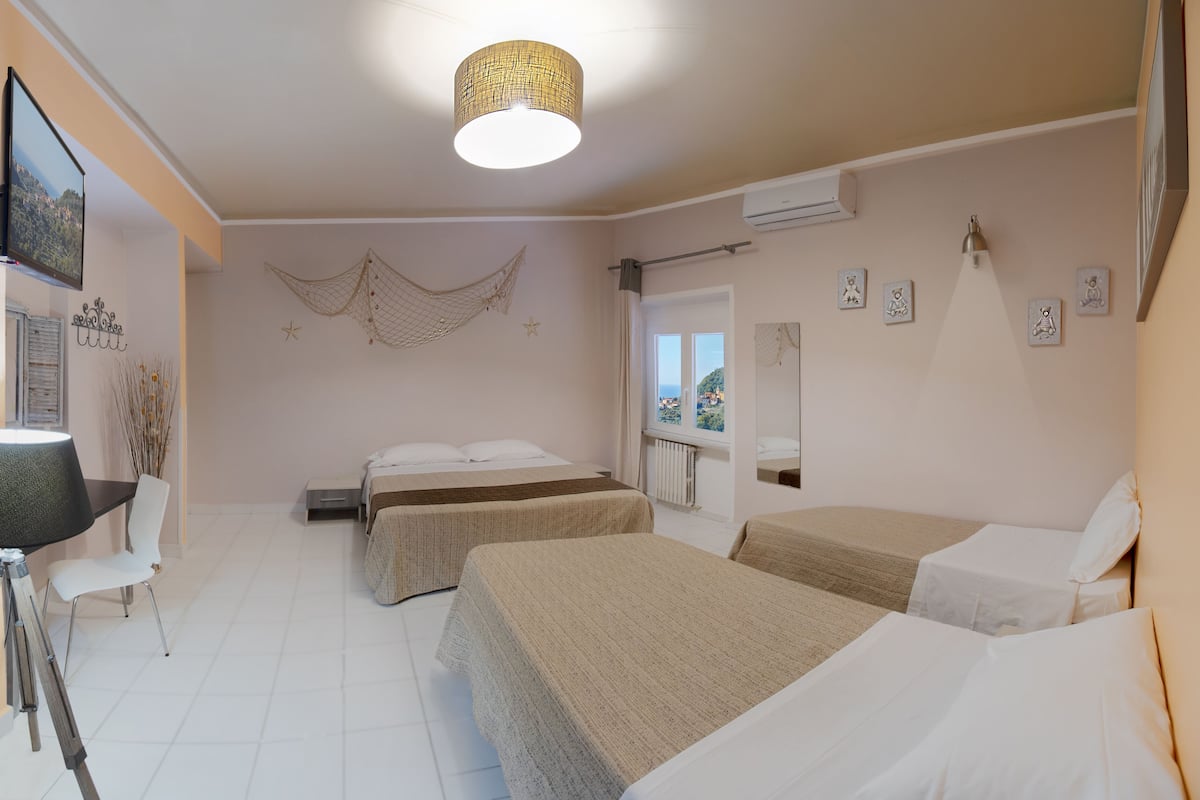 A hotel room with two single beds, a desk with a chair, a television, and a large window with a view.