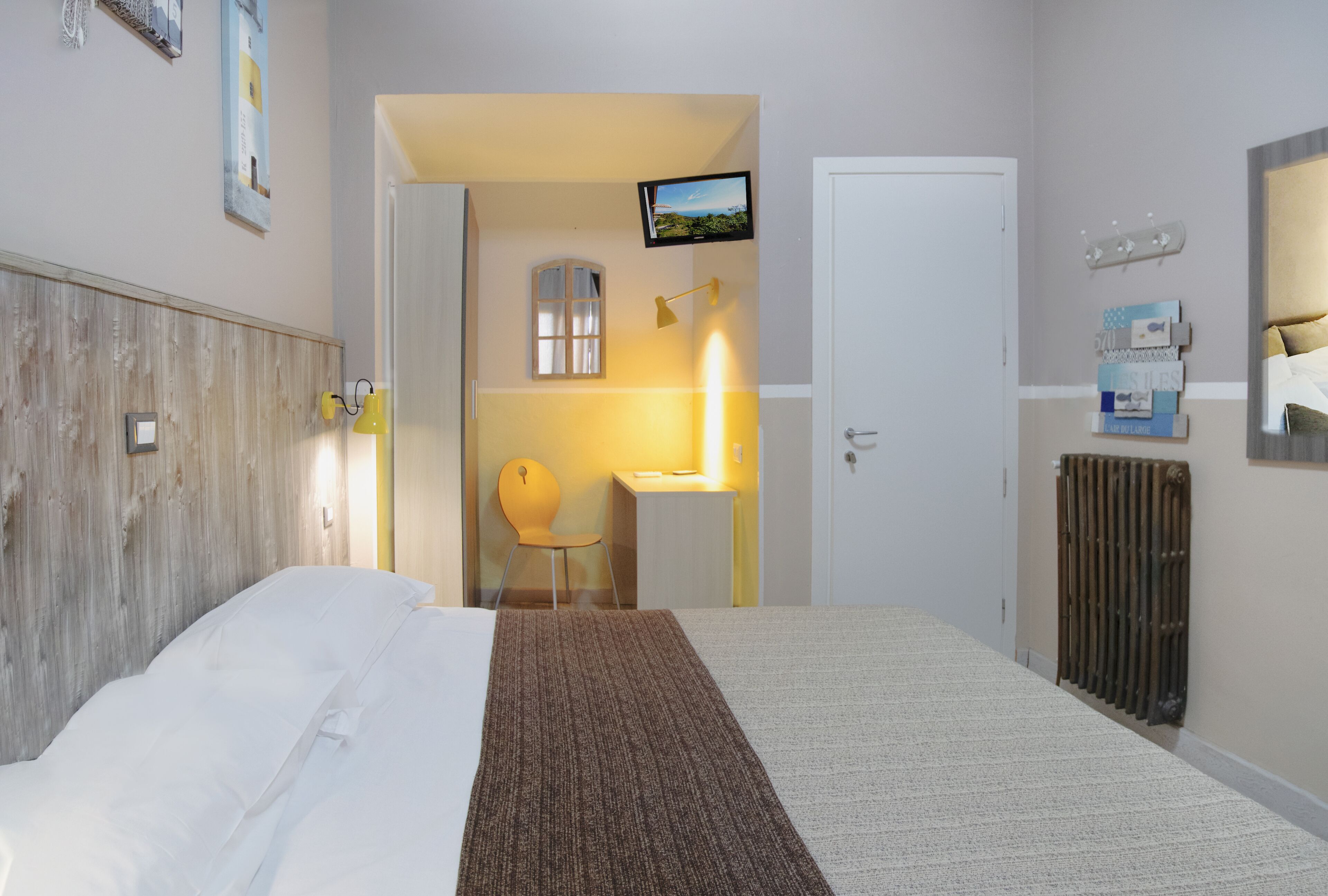 Una camera d'albergo con un letto, una scrivania, una sedia, una TV, un termosifone e una finestra.