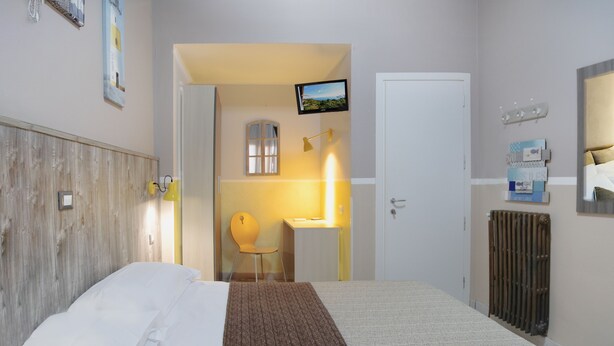 A hotel room with a bed, a desk, a chair, a TV, a radiator, and a window. - Albergo Serena (Arcola)