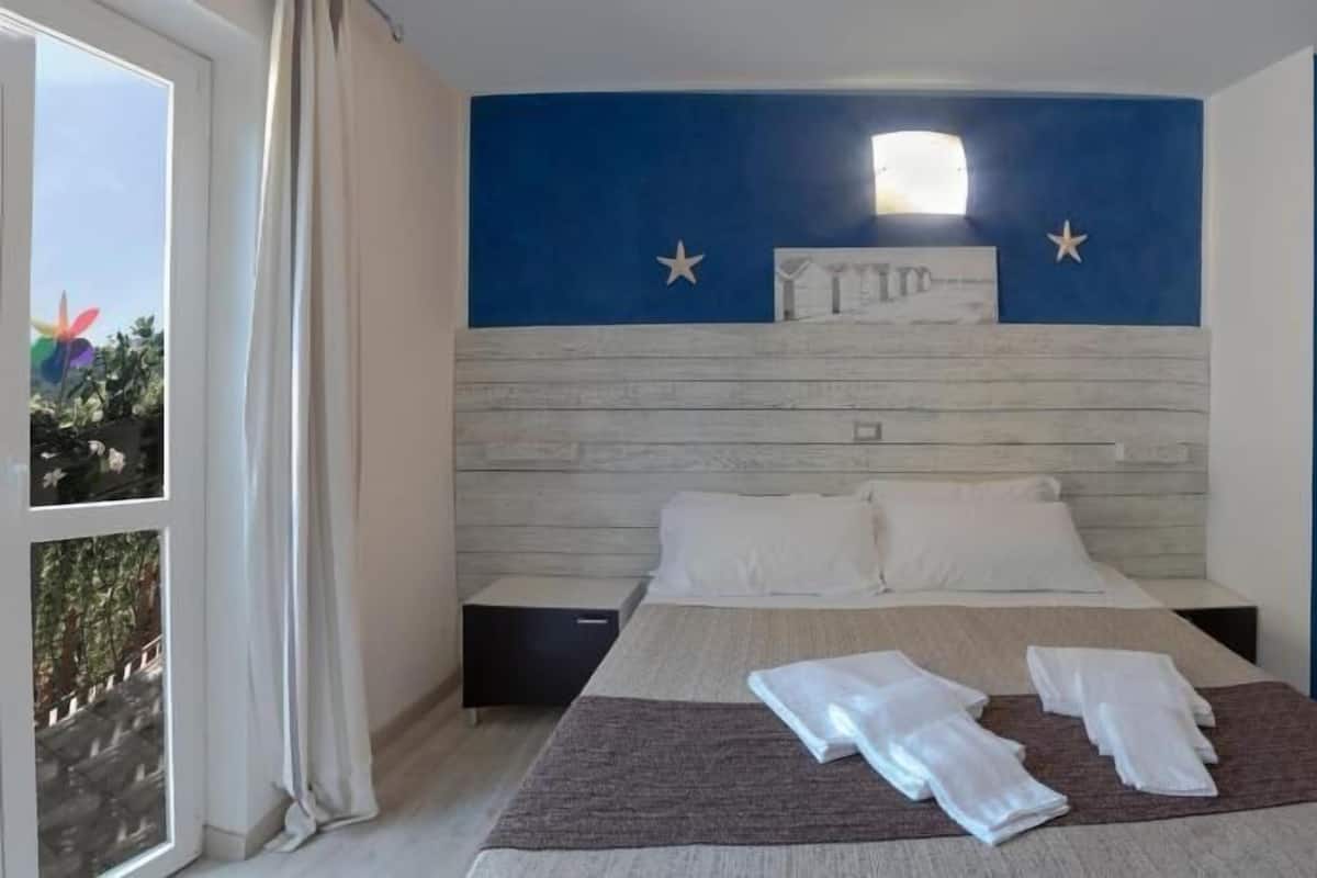 A bedroom with a bed, two pillows, a nightstand, a window with curtains, and a wall with a star and a net design.