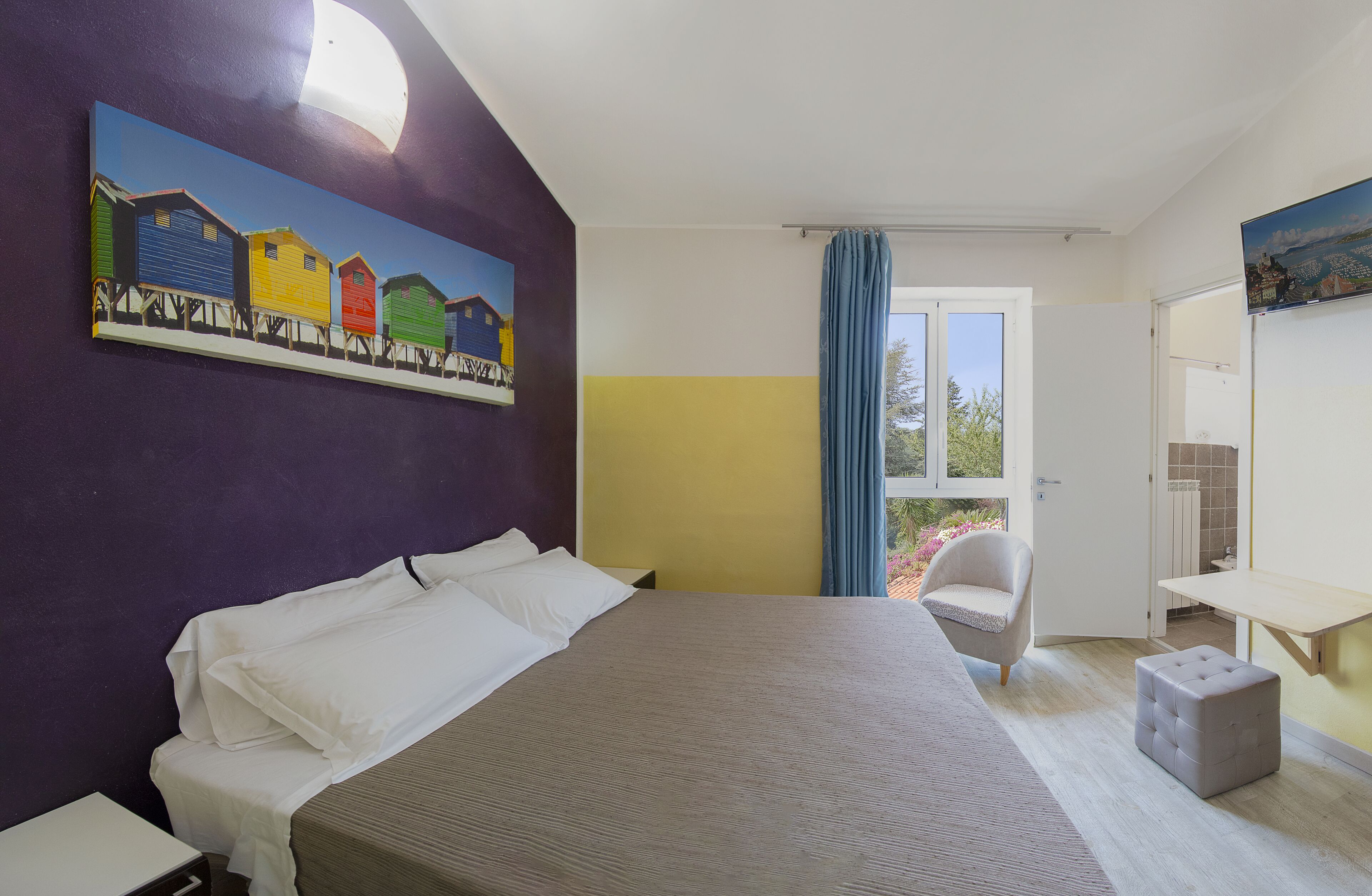 A bedroom with a bed, a chair, a small table, a painting on the wall, and a view through a window.