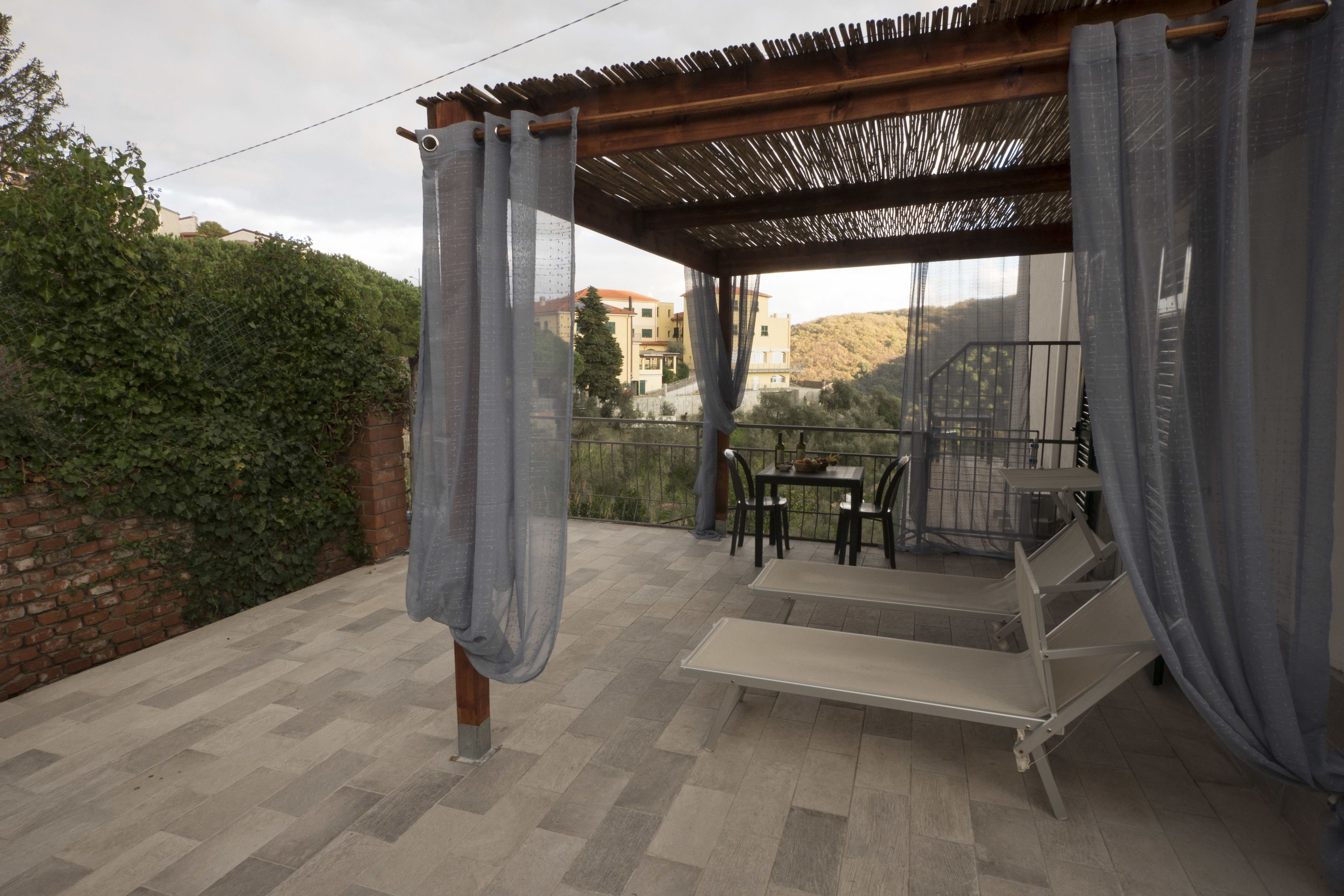 Un espace extérieur abrité, aménagé avec une table et des chaises, un banc, et offrant une vue sur une colline.