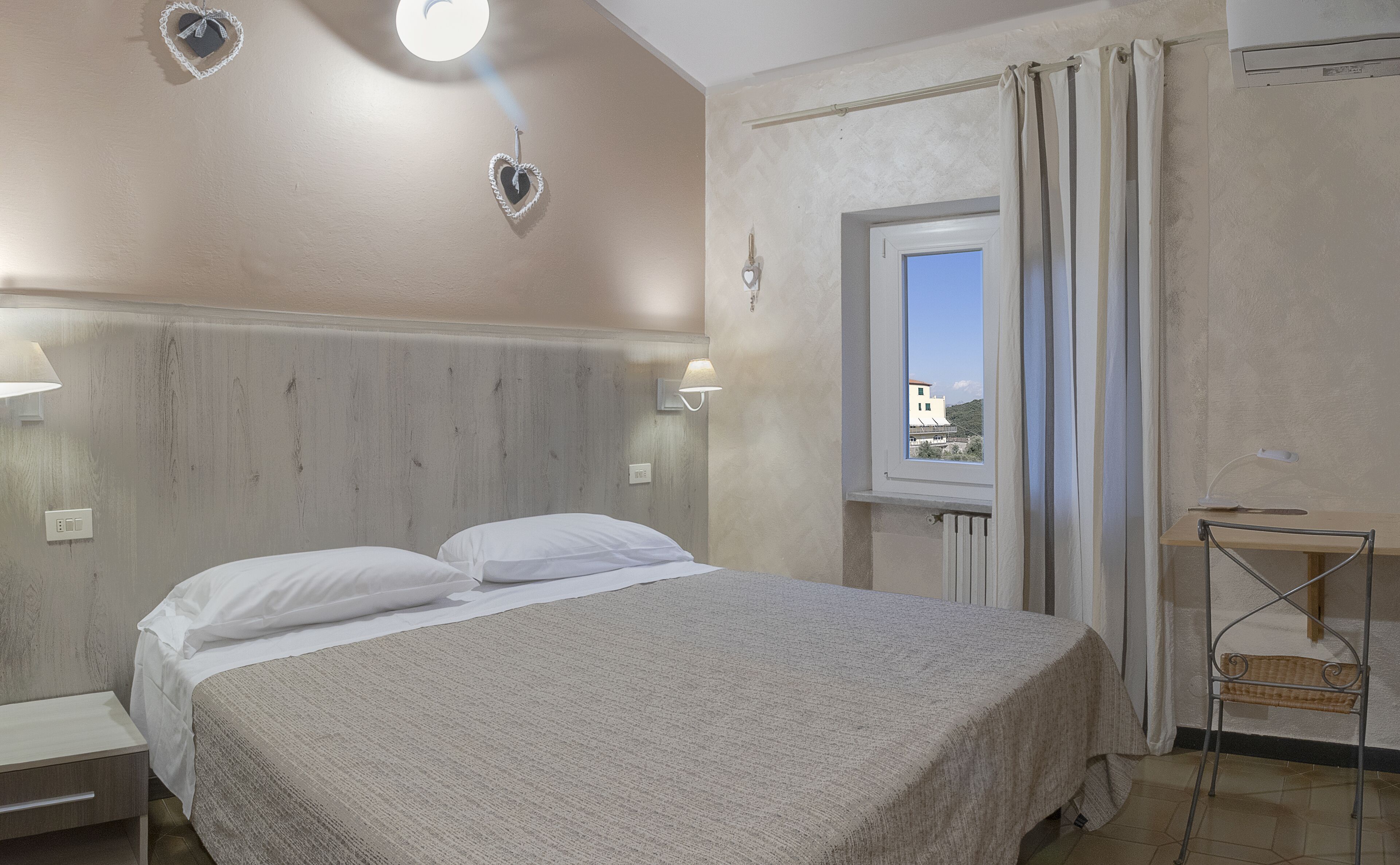 Une chambre à coucher avec un lit, des lampes de chevet, une fenêtre et une vue sur un bâtiment à l’extérieur.