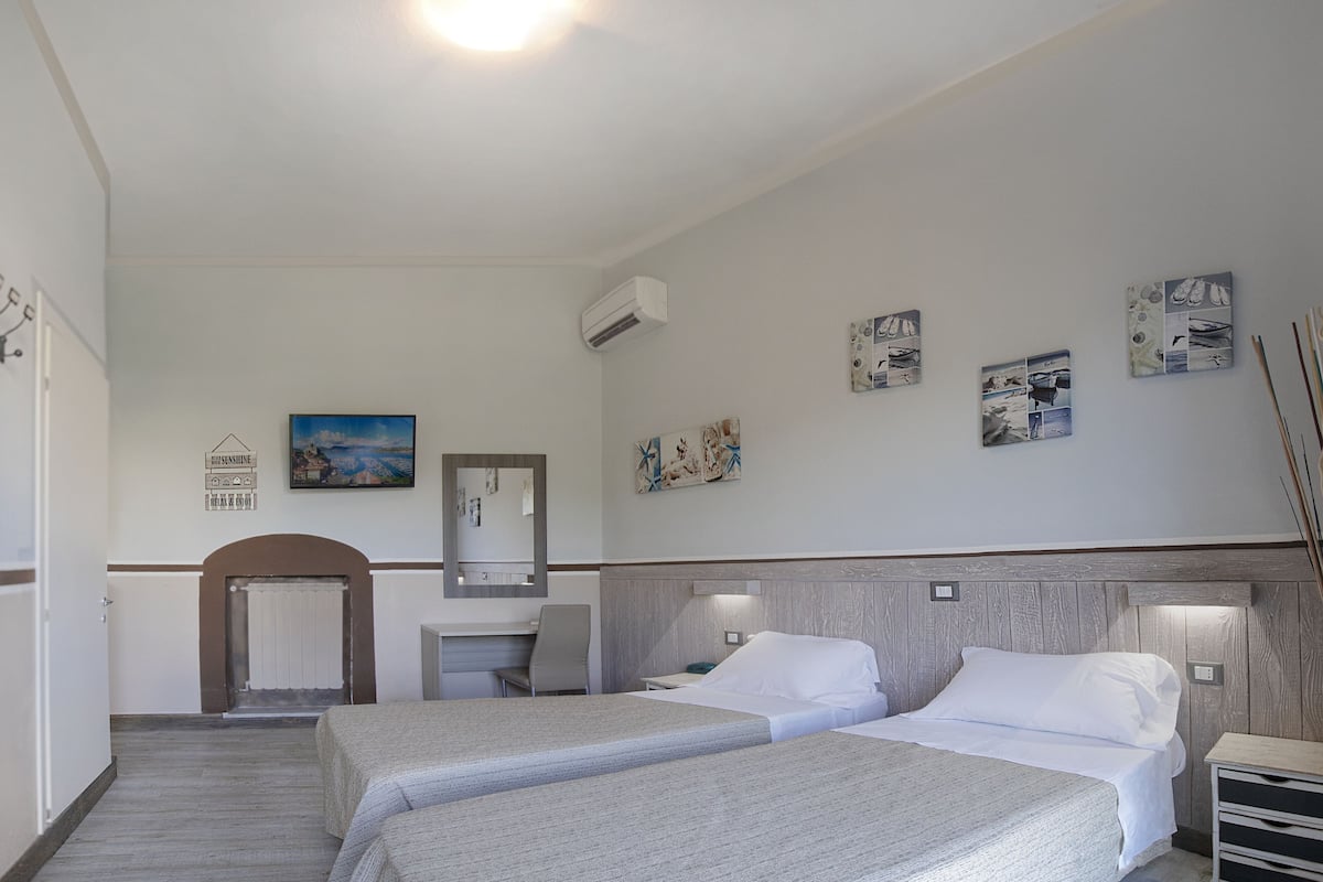 A hotel room with two beds, a desk, a chair, a mirror, and wall art.