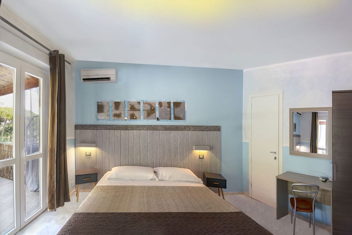 A bedroom with a bed, bedside tables, a desk, a chair, a mirror, and a window.