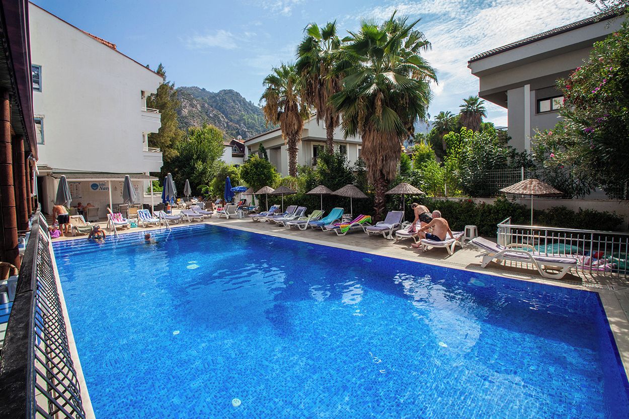 Une piscine entourée de bâtiments et de palmiers, avec des chaises longues et des parasols.