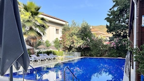 A swimming pool with lounge chairs and umbrellas, surrounded by greenery and a building. - Navy Hotel (Marmaris)
